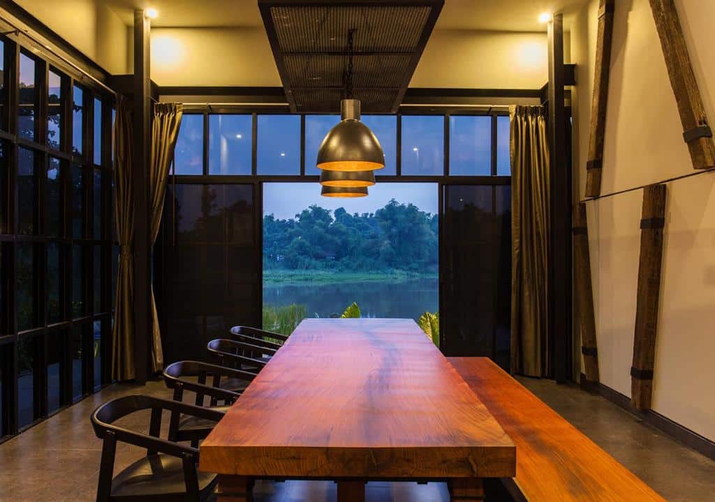 ห้องรับประทานอาหารพร้อมโต๊ะและเก้าอี้ไม้ขนาดใหญ่ ตั้งอยู่ในรีสอร์ทริมแม่น้ำในจังหวัดราชบุรี ที่พักราชบุรีริมน้ำ