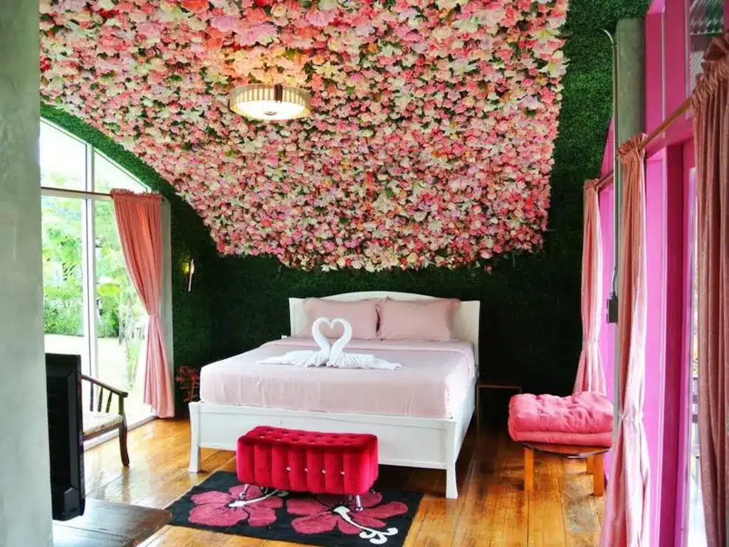 ห้องนอนตกแต่งด้วยดอกไม้สีชมพูบนเพดาน ตั้งอยู่ในโรงแรมริมแม่น้ำในจังหวัดราชบุรี ล้อมรอบด้วยธรรมชาติอันงดงาม โรงแรมในราชบุรี