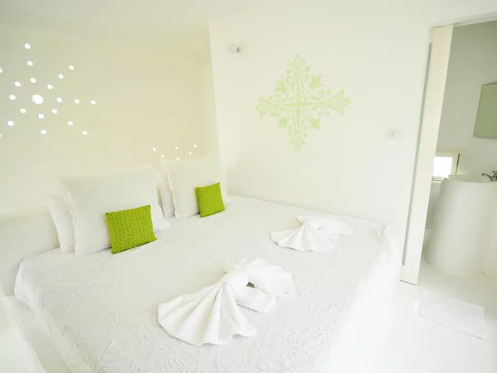 เตียงสีขาวพร้อมผ้าเช็ดตัวสีเขียวที่โรงแรมริมแม่น้ำในจังหวัดราชบุรี ที่พักริมน้ำราชบุรี