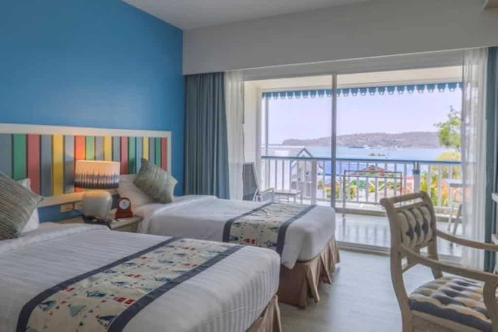 เตียงสองเตียงในห้องที่มีผนังสีฟ้าและมองเห็นวิวทะเลในพื้นที่ท่องเที่ยวราชบุรี ที่พักเกาะสีชัง