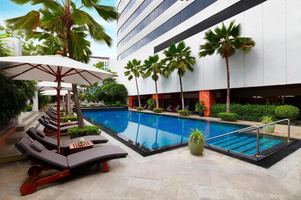 สระว่ายน้ำพร้อมเก้าอี้นั่งเล่นและร่มหน้าอาคารในอุทยานราชบุรี ที่พักกรุงเทพ
