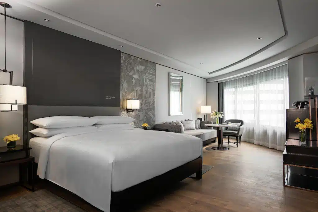  ที่พักกรุงเทพ       ราชบุรีที่เที่ยว: ห้องพักในโรงแรมที่มีเตียงสีขาวและพื้นไม้ในราชบุรี
