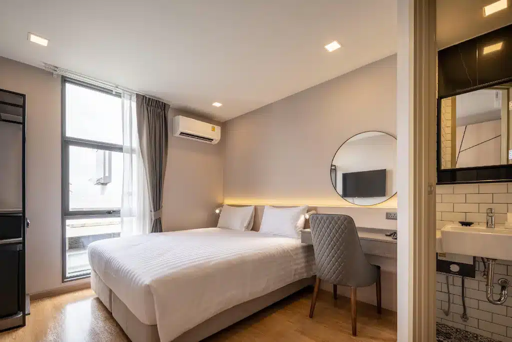ห้องพักพร้อมเตียง อ่างล้างหน้า และกระจก สำหรับนักเดินทางมาเยือนชัยนาท โรงแรมกรุงเทพ หรือราชบุรี