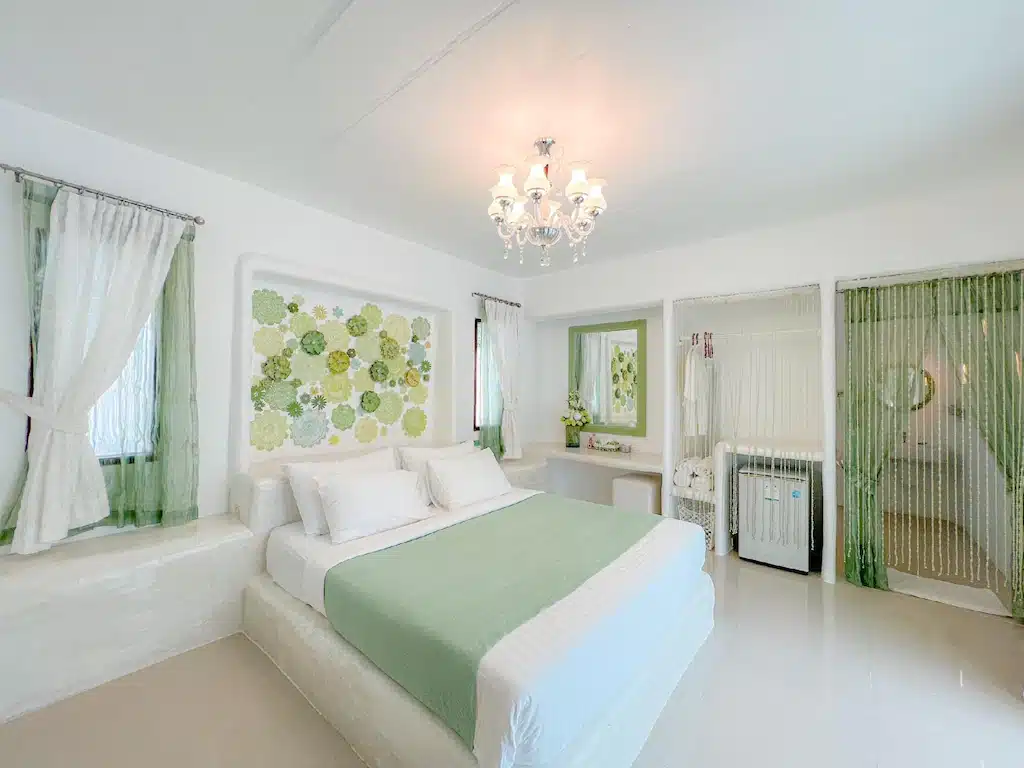 ห้องนอนอันเงียบสงบตกแต่งด้วยโคมระย้ามีสไตล์และผสมผสานกับเฉดสีขาวและเขียวอันสดชื่น ที่พักราชบุรีธรรมชาติ