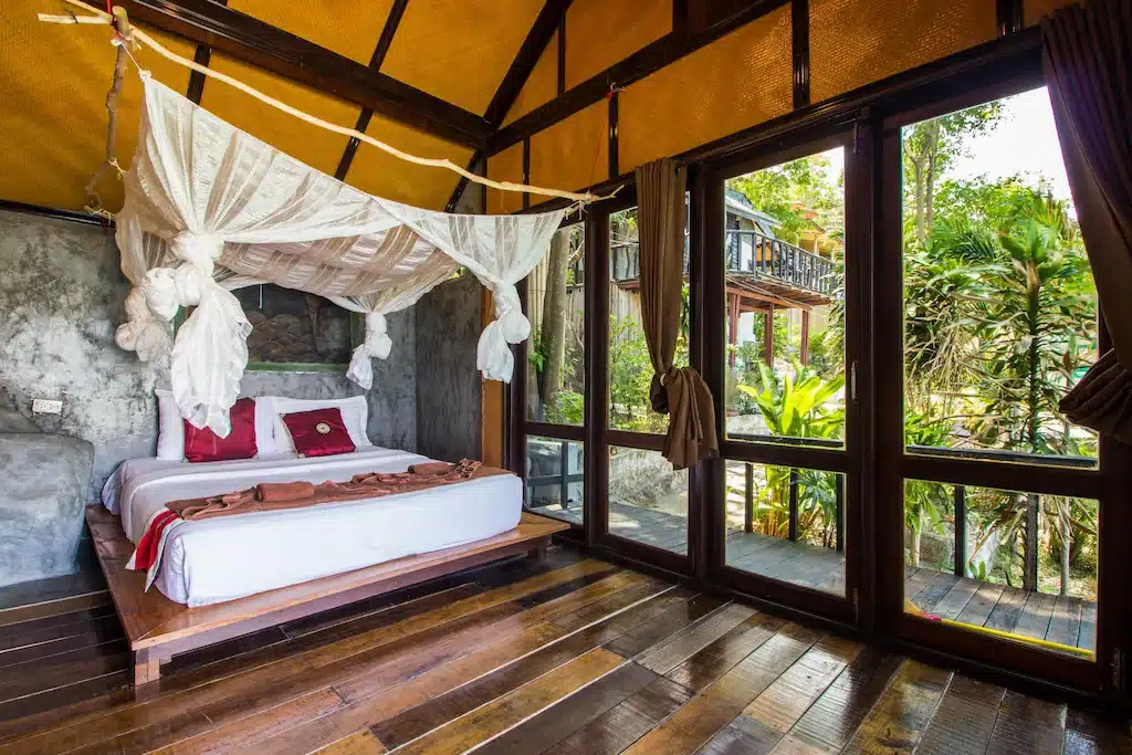 ห้องนอนพร้อมเตียงกระโจมและพื้นไม้ในสถานที่พักผ่อนอันมีเสน่ห์แห่งราชบุรี ที่พักเกาะเต่า