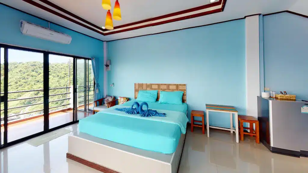 เตียงในห้องที่มีผนังสีฟ้าและระเบียง ที่พักเกาะสีชัง
