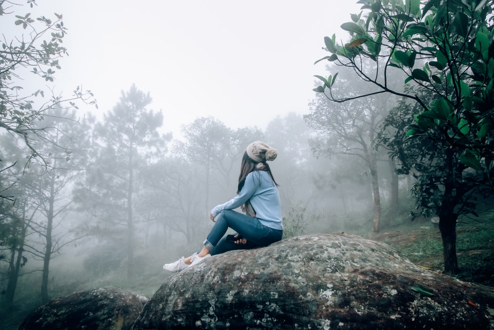 ผู้หญิงนั่งอยู่บนก้อนหินในป่าอันเงียบสงบ ที่เที่ยวเลย