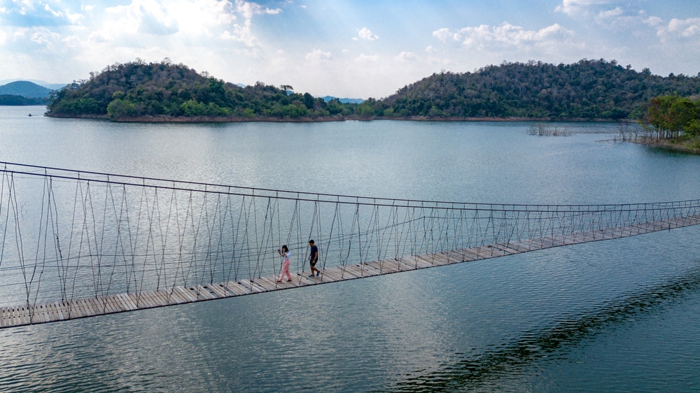 คู่รักกำลังเดินอยู่บนสะพานแขวนเหนือทะเลสาบ ที่เที่ยวชะอำ