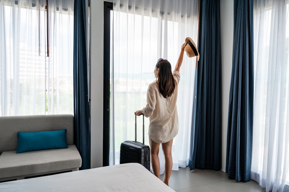 ผู้หญิงคนหนึ่งยืนอยู่หน้าหน้าต่างในห้องพักของโรงแรมพร้อมทิวทัศน์อันสวยงามของทะเล (ทะเล) ที่พักอ่าวนางติดทะเล