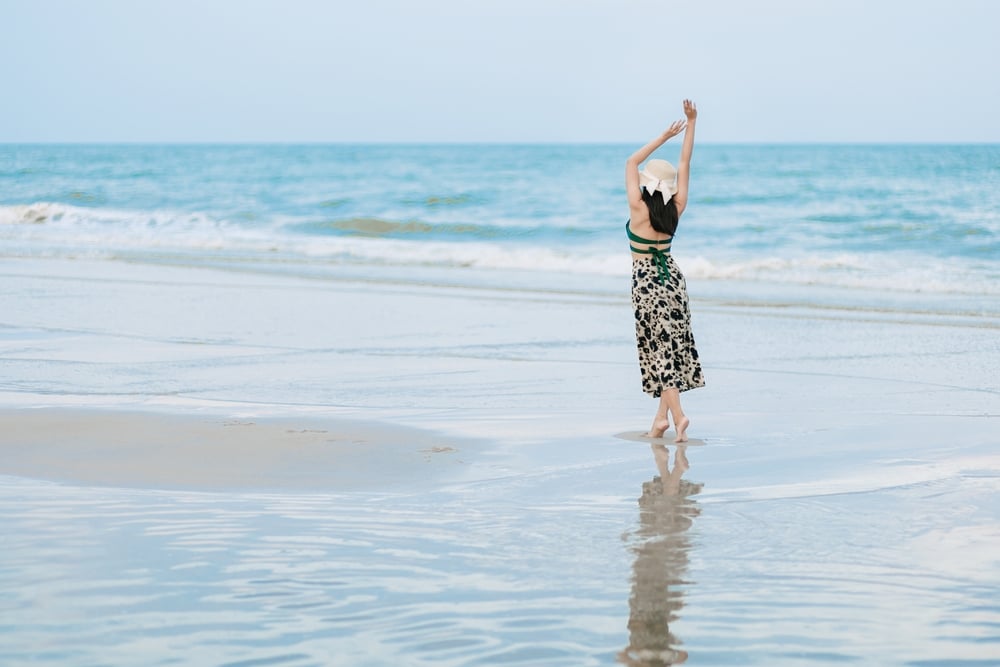 ผู้หญิงยืนอยู่บนชายหาดโดยยกแขนขึ้นในบริเวณที่ท่องเที่ยวราชบุรี