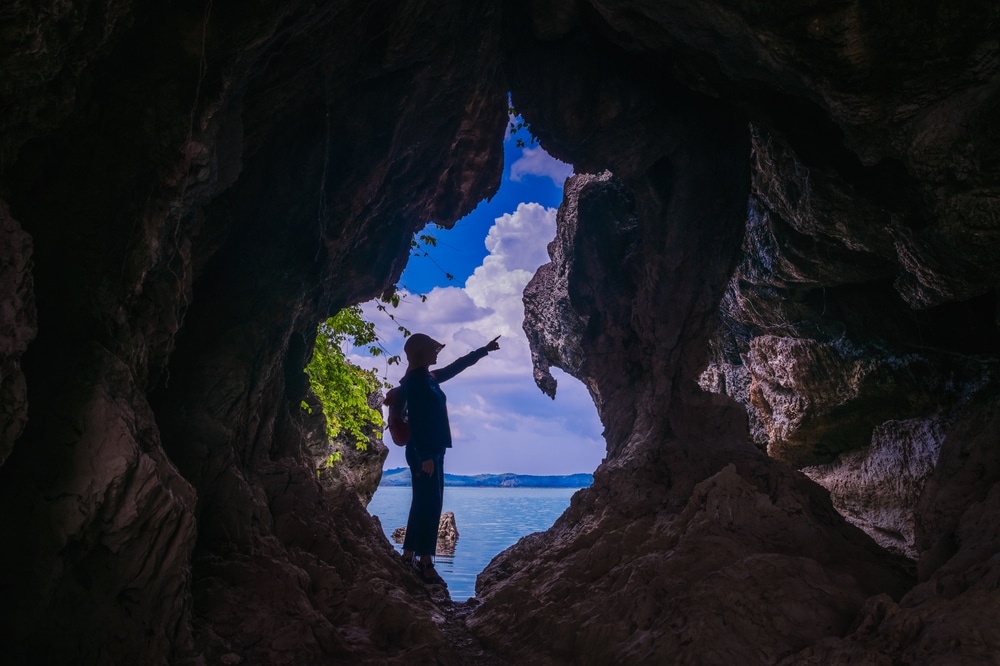 ชายคนหนึ่งยืนอยู่ในถ้ำมองดูมหาสมุทรในบริเวณที่ท่องเที่ยวราชบุรี ที่เที่ยวพัทลุง