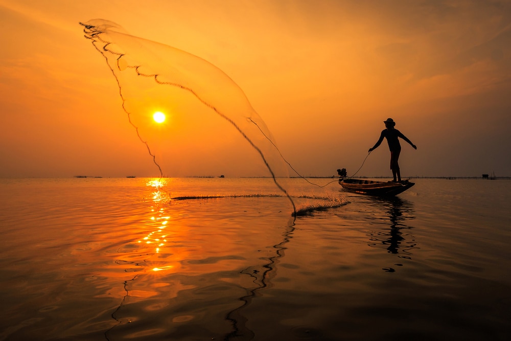 ผู้ชายกำลังตกปลาในเรือตอนพระอาทิตย์ตกใกล้กับที่เที่ยวชัยนาท ที่เที่ยวหาดใหญ่