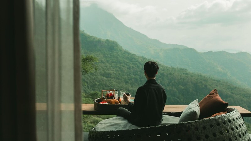 ผู้ชายกำลังนั่งอยู่บนระเบียงที่มองเห็นภูเขา ที่พักเขาค้อ