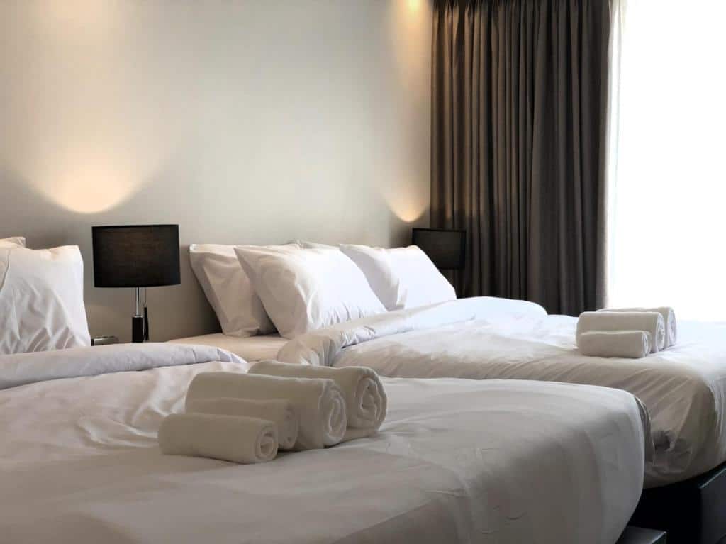 เตียงสองเตียงพร้อมผ้าปูที่นอนสีขาวและผ้าเช็ดตัวในห้องพักโรงแรมในราชบุรีที่เที่ยว