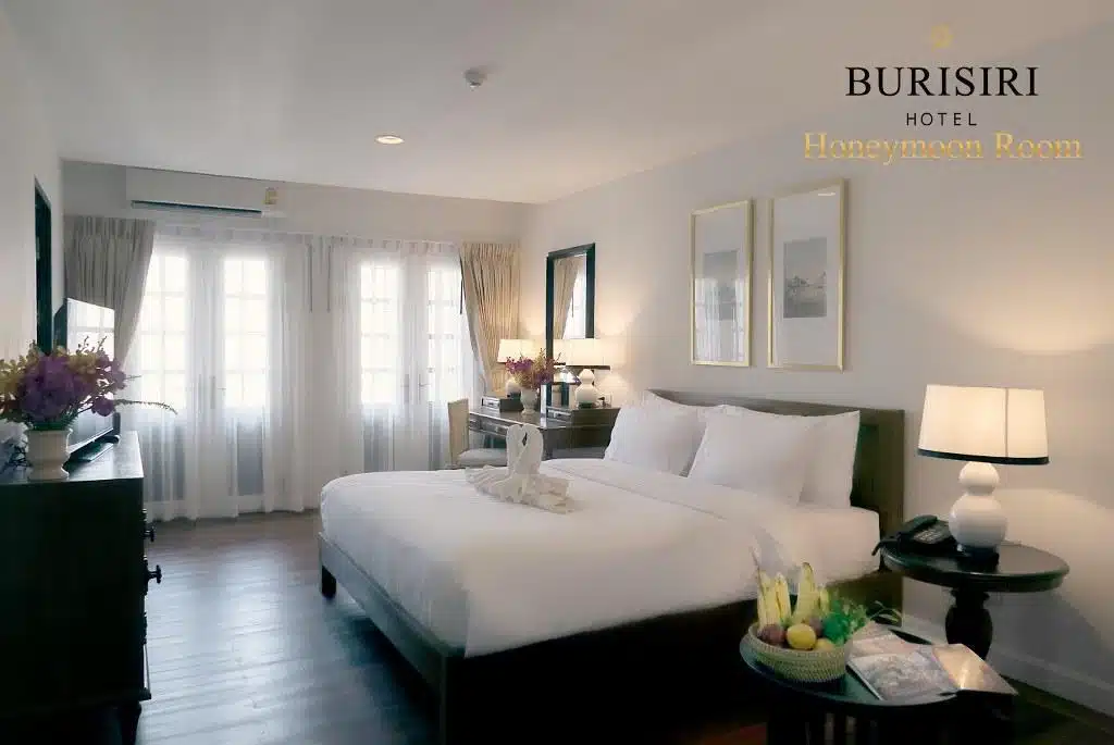 ห้องพักในโรงแรมพร้อมเตียงและโต๊ะข้างเตียง เหมาะสำหรับนักเดินทางที่สำรวจราชบุรี โรงแรมเชียงใหม่