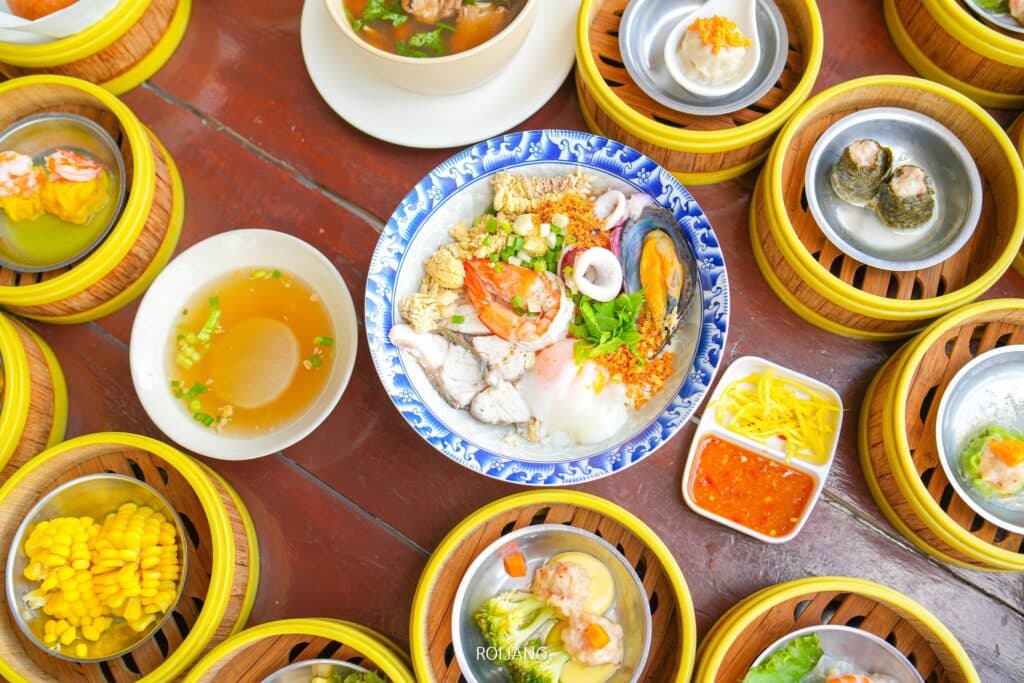 อาหารหลายชามบนโต๊ะไม้แสดงถึงรสชาติอันเย้ายวนของติ่มซำภูเก็ต ติ่มซำภูเก็ต