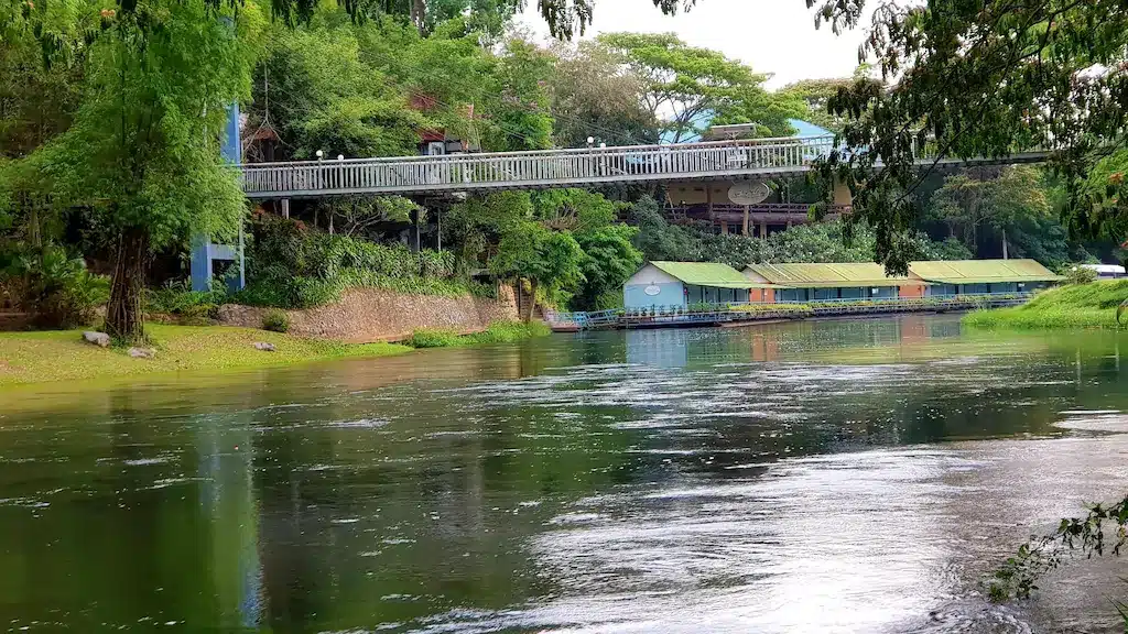 สะพานข้ามแม่น้ำในพื้นที่สีเขียวที่ล้อมรอบด้วยทิวทัศน์ที่สวยงามของชุมพรติดทะเล โรงแรมแก่งกระจาน