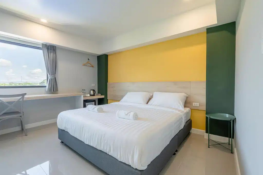 เตียงในห้องที่มีผนังสีเหลืองเน้นสีเหลือง เหมาะสำหรับการเข้าพักสบายๆ ใกล้แม่น้ำแม่คำ จังหวัดลำปาง ที่พักกว๊านพะเยา