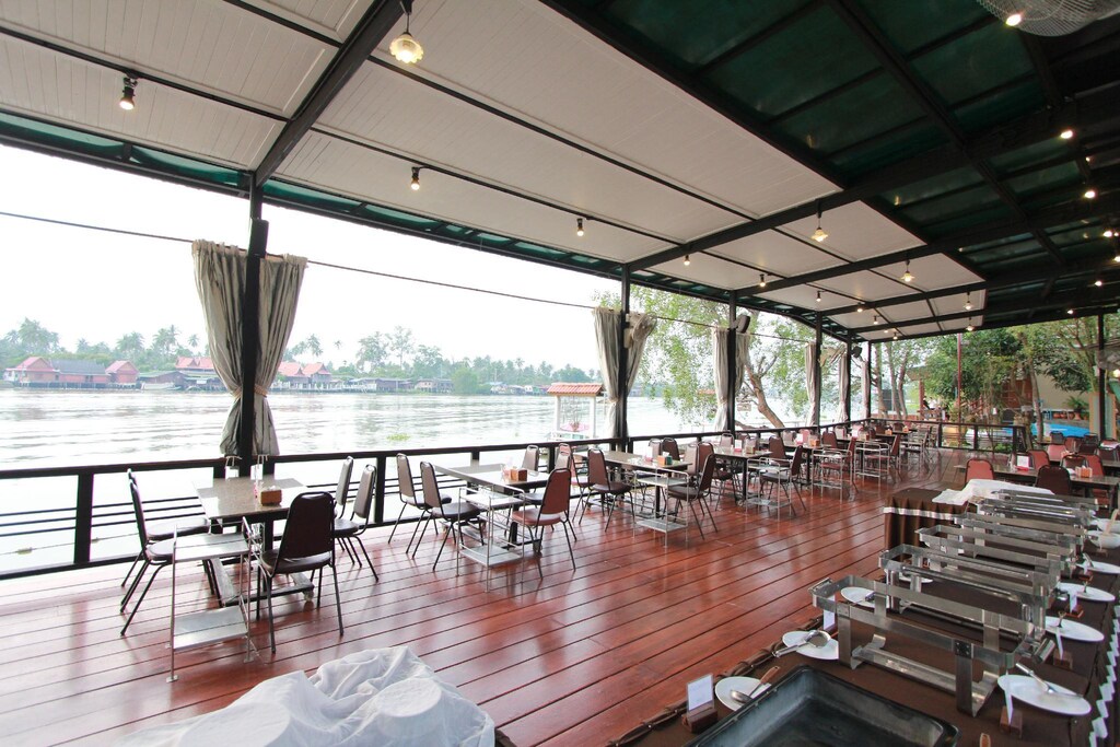ร้านอาหารพร้อมโต๊ะและเก้าอี้ที่มองเห็นวิวแม่น้ำ โรงแรมอัมพวา