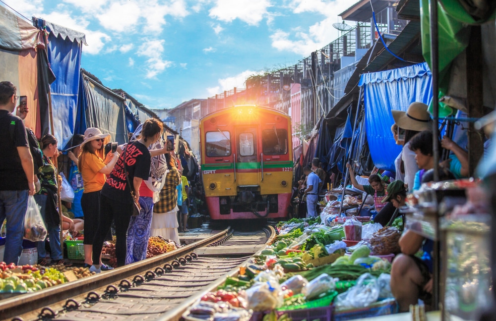 รถไฟกำลังแล่นผ่านตลาดอันคึกคักใกล้กับตลาดที่มีร่มเงา ตลาดร่มหุบ