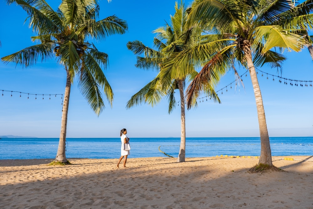 ผู้หญิงกำลังเดินอยู่บนชายหาดพร้อมต้นปาล์มในปาปา ที่เที่ยวเด็กพัทยา