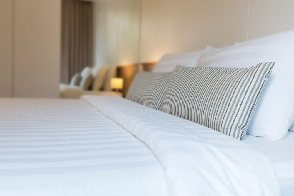 ห้องพักในโรงแรมที่มีเตียงประดับด้วยผ้าปูที่นอนและหมอนสีขาว ที่พักแก่งกระจานริมน้ำ
