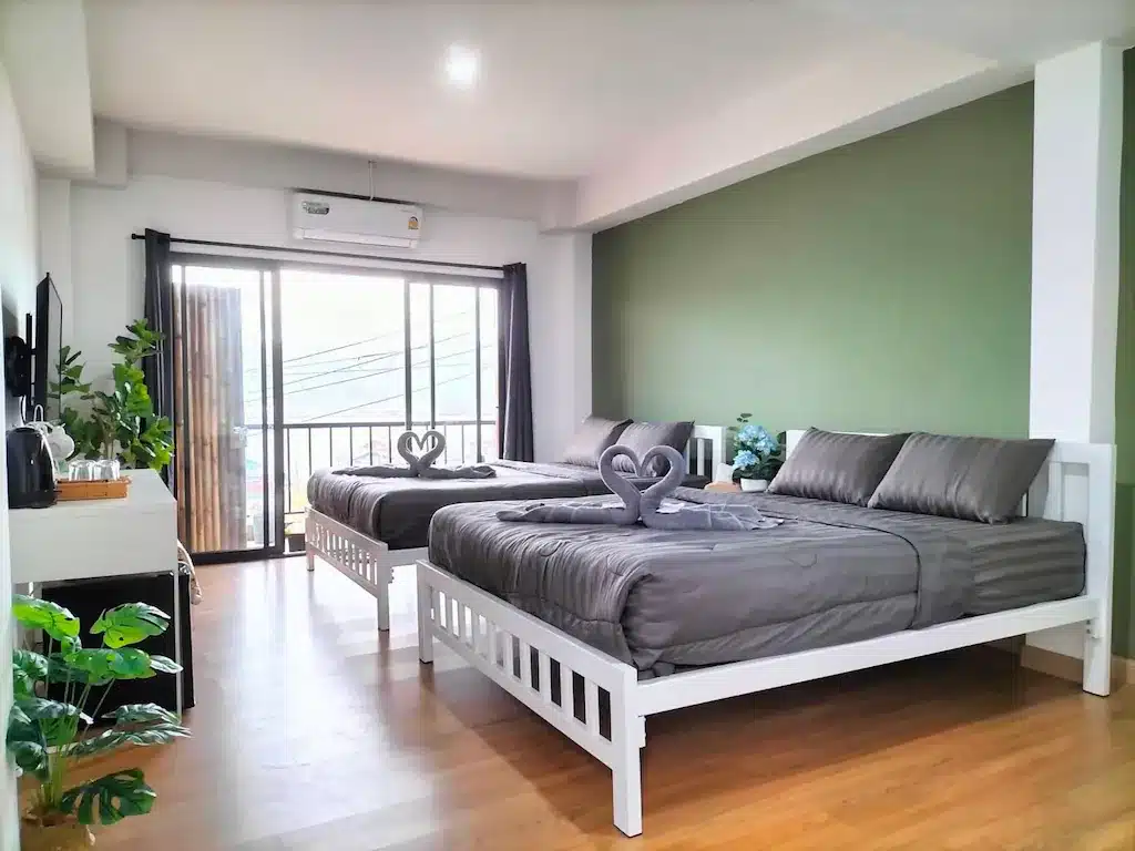 สองเตียงในห้องที่มีผนังสีเขียวและระเบียงที่สังขละบุรี อ ที่พักสังขละบุรี