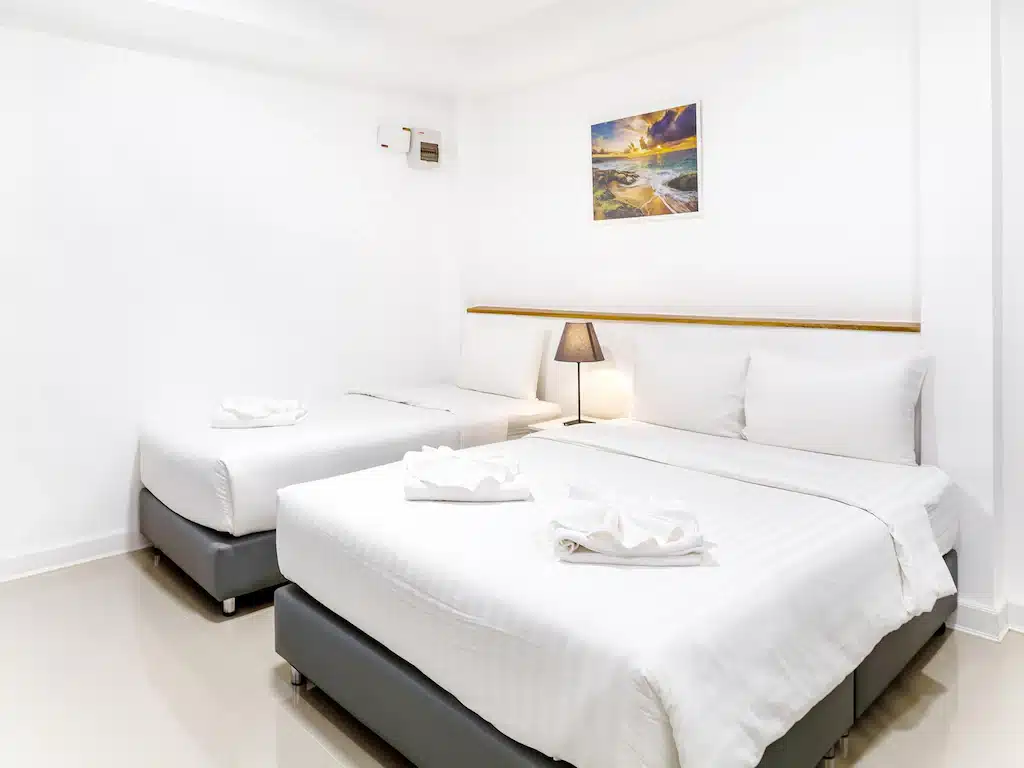 สองเตียงในห้องพร้อมผ้าปูที่นอนสีขาวและผ้าเช็ดตัว ใกล้สถานที่ท่องเที่ยวราชบุรี ที่เที่ยวสัตหีบ