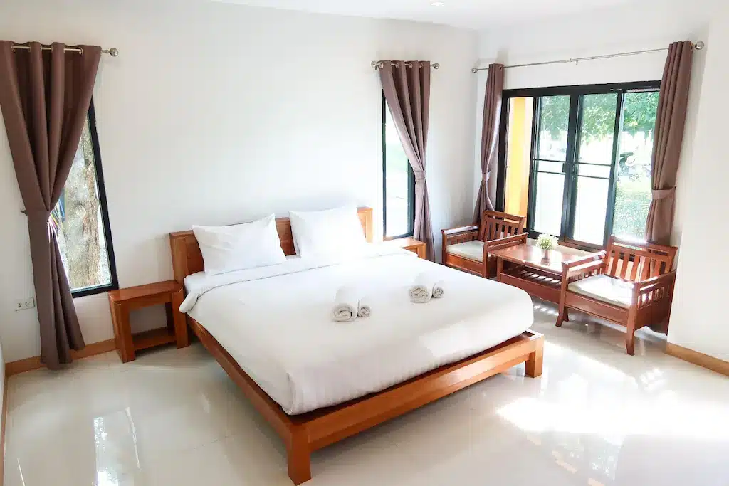 ห้องนอนพร้อมเตียงสีขาวและเฟอร์นิเจอร์ไม้ในราชบุรีที่เที่ยว  ชุมพรที่เที่ยว