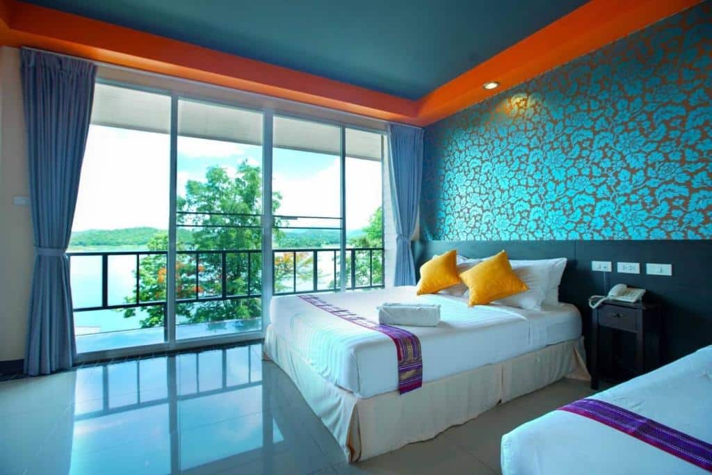 เตียงสองเตียงในห้องที่มีผนังสีฟ้าและสีส้ม เหมาะสำหรับนักเดินทางที่มาเยือนน่าน ที่พักใกล้สะพานมอญสังขละบุรีราคาถูก