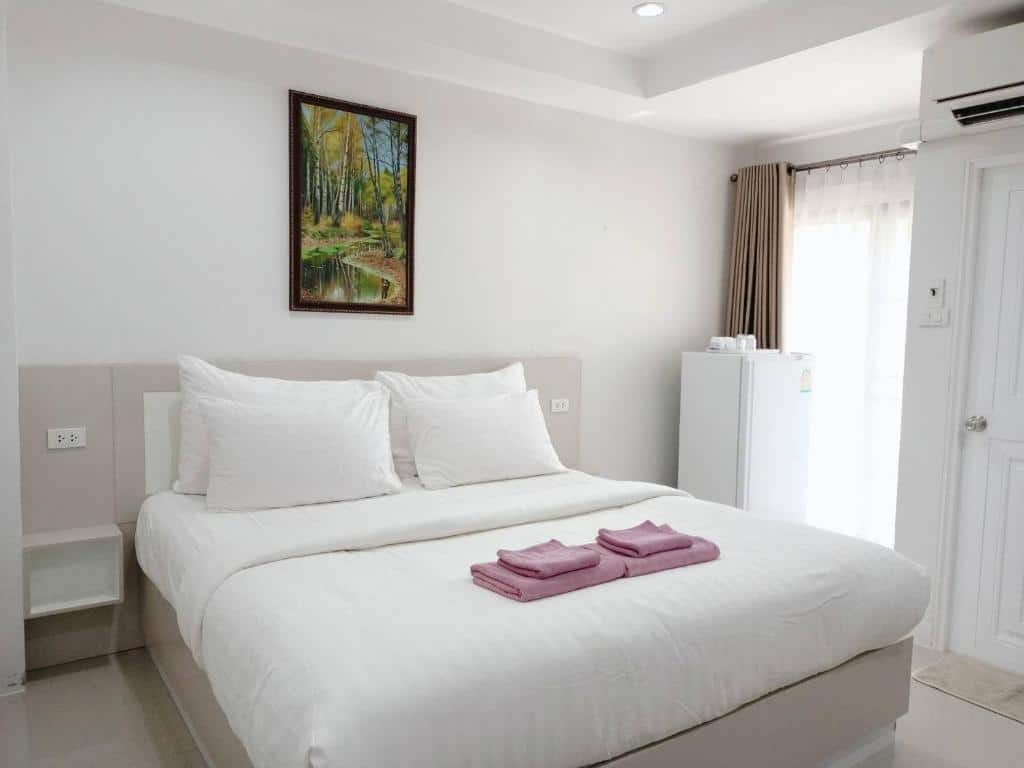 ห้องนอนที่มีเตียงสีขาวและผ้าเช็ดตัวสีชมพูอยู่ในสถานที่ท่องเที่ยวน่าน โรงแรมสุรินทร์