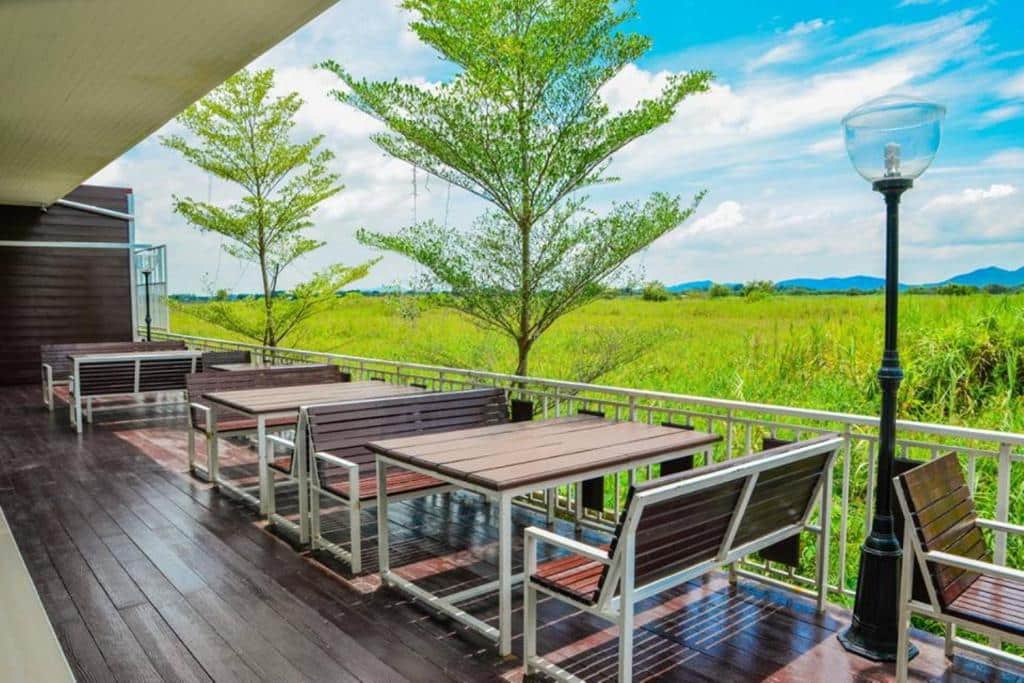 ดาดฟ้าไม้พร้อมโต๊ะและเก้าอี้ที่มองเห็นทุ่งหญ้าในเที่ยวน่าน ที่พักสังขละบุรี