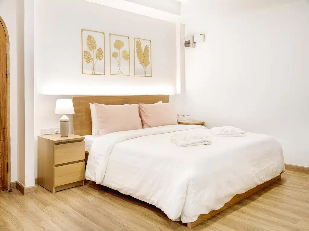 ห้องนอนพร้อมเตียงสีขาวบนพื้นไม้ในราชบุรีที่เที่ยว ที่เที่ยวสัตหีบ