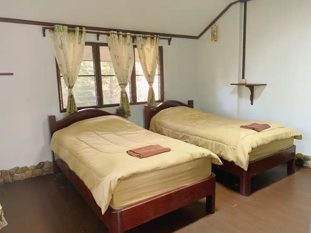 สองเตียงในห้องที่มีพื้นไม้ในข้อมูลท่องเที่ยวน่าน ที่พักสังขละบุรี