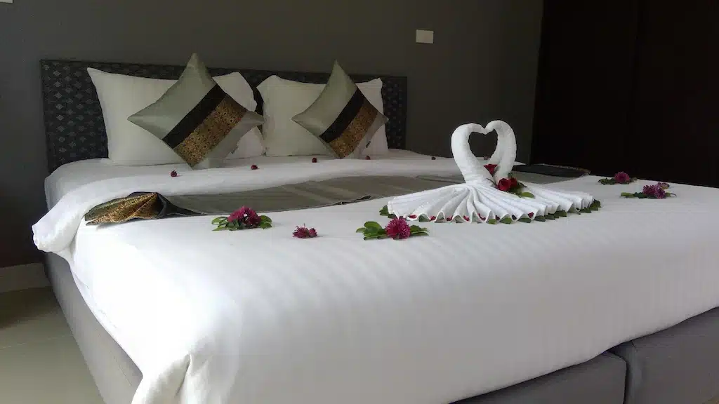 เตียงสีขาวที่มีดอกไม้และผ้าเช็ดตัวอยู่บนเตียงในรีสอร์ทริมทะเล ที่พักเขาหลักติดทะเล