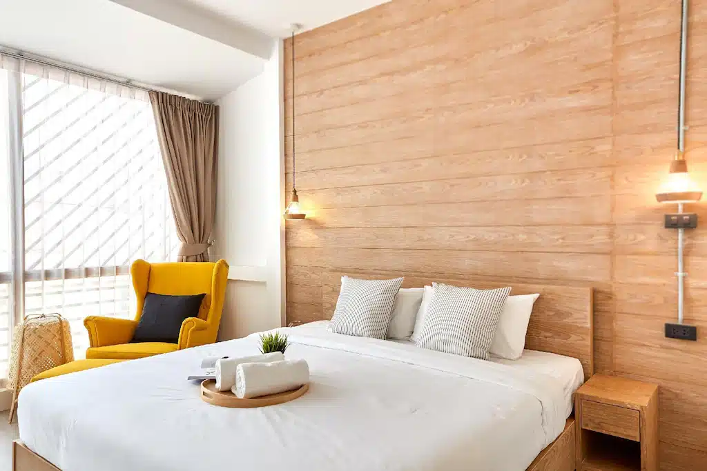เตียงในห้องที่มีผนังไม้และเก้าอี้สีเหลืองในพูลวิลล่าหัวหินติดทะเล บ้านพักติดทะเลหัวหิน