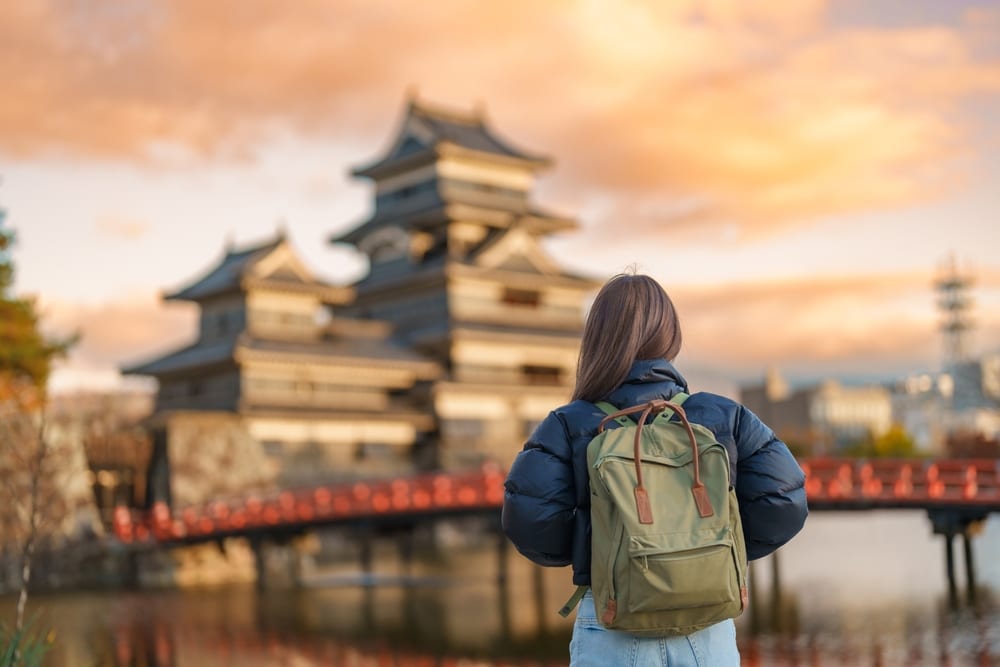 ผู้หญิงสะพายเป้ยืนอยู่หน้าปราสาทญี่ปุ่น ซึ่งเป็นสถานที่ท่องเที่ยวยอดนิยมในญี่ปุ่น เที่ยวญี่ปุ่น