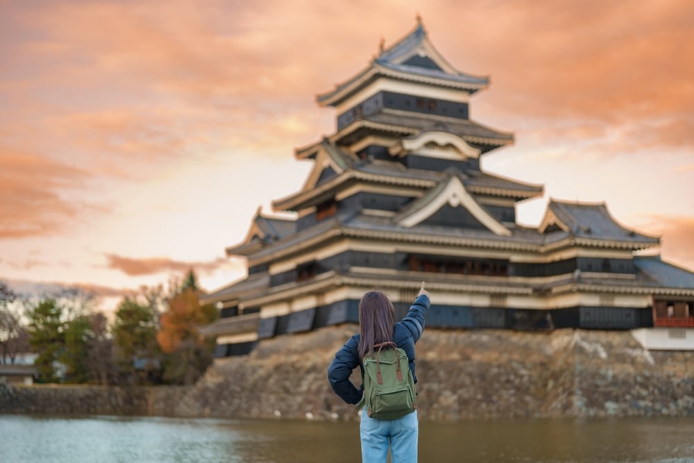 ผู้หญิงคนหนึ่งยืนอยู่หน้าปราสาทญี่ปุ่น ซึ่ เที่ยวญี่ปุ่น เป็นสถานที่ท่องเที่ยวยอดนิยมในญี่ปุ่น