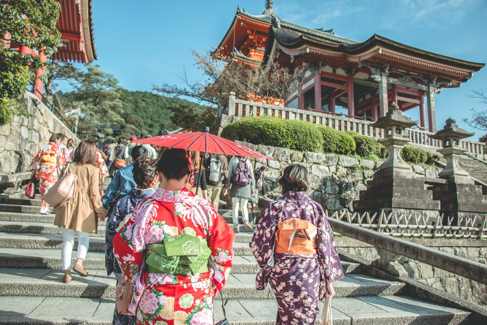 กลุ่มคนเดินขึ้นบันไดพร้อมร่มสีแดงที่จุดท่องเที่ยวในญี่ปุ่น เที่ยวญี่ปุ่นด้วยตัวเอง
