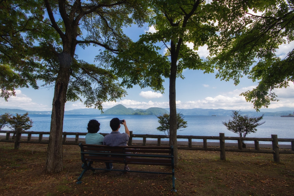 คนสองคนนั่งอยู่บนม้านั่งที่สถานที่ท่องเที่ยวราชบุรี เที่ยวญี่ปุ่น