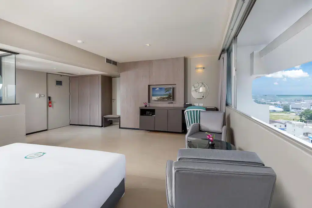 ห้องพักโรงแรมทันสมัย ดีไซน์มินิมอล มีเตียงขนาดใหญ่ พื้นที่นั่งเล่น และหน้าต่างแบบพาโนรามาพร้อมวิว ถนนคนเดินภูเก็ต
