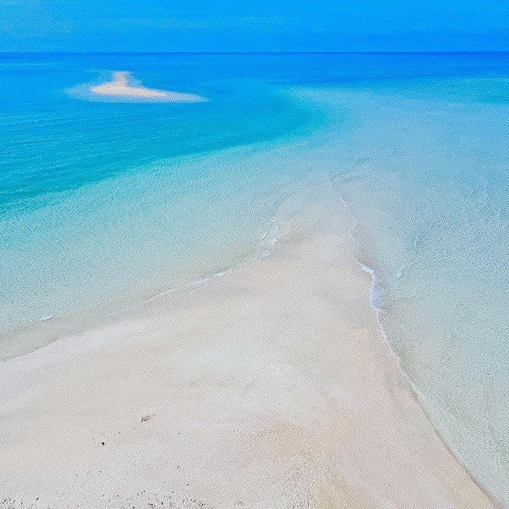 หาดทรายชายฝั่งในพังงา น้ำทะเลสีฟ้าใส ใต้ท้องฟ้าสดใส มีสันทรายเล็กๆ อยู่ไกลๆ