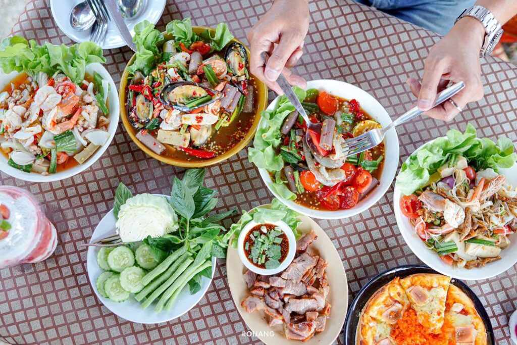 คนหนึ่งกำลังรับประทานอาหารที่โต๊ะพร้อมอาหารไทยต่างๆ ในพังงา ทั้งสลัด ซุป และอาหารทะเล พร้อมรับประทานด้วยส้อมและช้อน