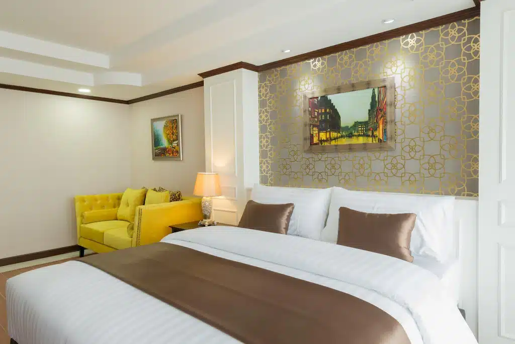 ห้องพักโรงแรมทันสมัยและตกแต่งอย่างดีพร้อมเตียงคู่ โซฟาสีเหลือง และงานศิลปะบนผนัง ตั้งอยู่ริมแม่น้ำโขงในจังหวัดมุกดาหาร ที่พักริมโขงมุกดาหาร