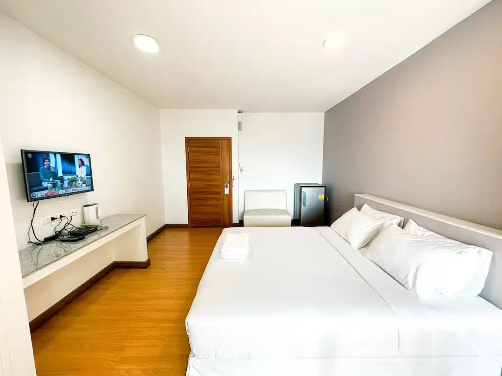 ห้องพักในโรงแรมสไตล์มินิมอลใกล้ตลาดบ้านเพ มีเตียงคู่ โทรทัศน์ติดผนัง และเฟอร์นิเจอร์เรียบง่าย ตลาดนัดเลียบด่วนรามอินทรา