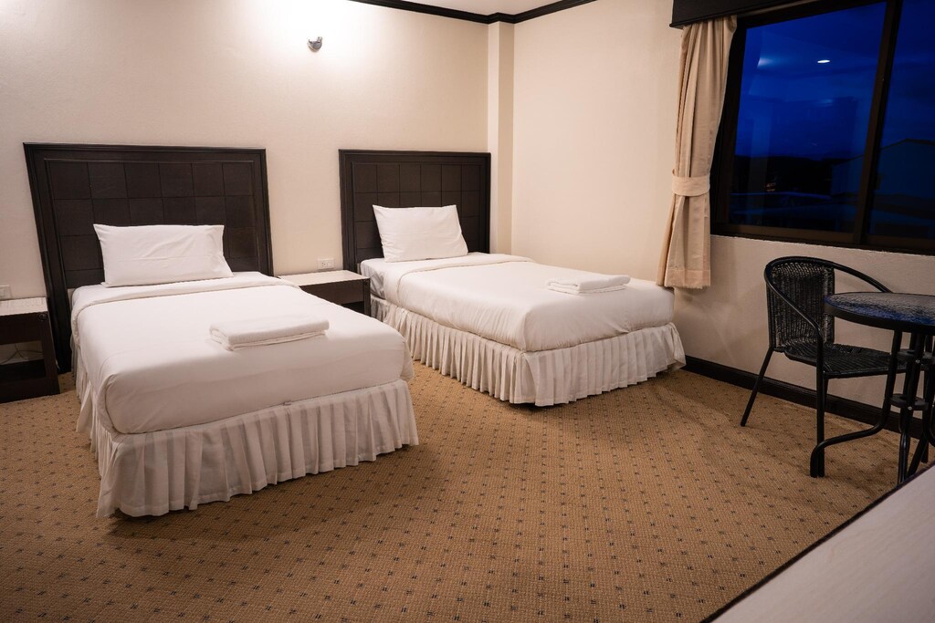 ห้องพักในโรงแรมที่มีเตียงแฝด 2 เตียงและโต๊ะเล็กๆ พร้อมเก้าอี้ริมหน้าต่างยามพลบค่ำ รีสอร์ทเบตง