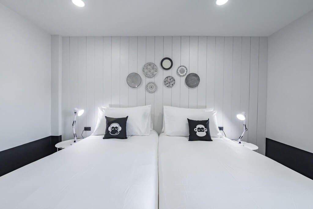ห้องนอนสไตล์มินิมอลพร้อมเตียงเดี่ยว 2 เตียง ชุดเครื่องนอนสีขาว แผ่นผนังตกแต่ง และโคมไฟข้างเตียง ที่พักบางแสน