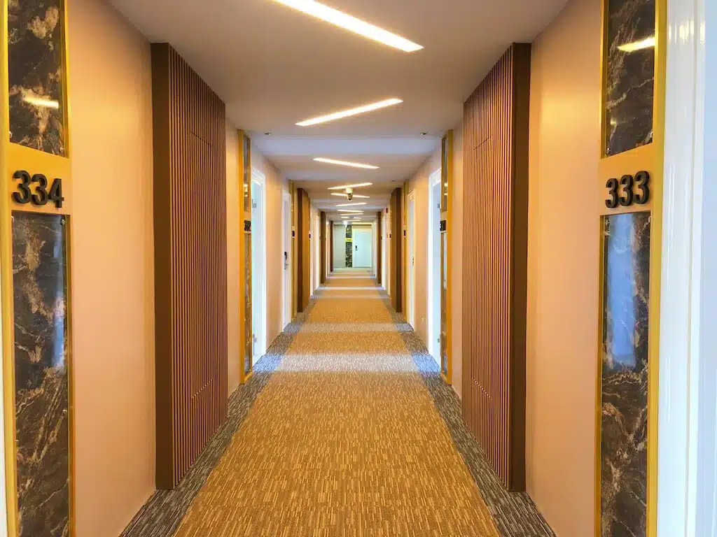 ทางเดินของโรงแรมที่มีพรมลวดลาย เชิงเทียนติดผนัง และประตูที่มีหมายเลขกำกับไปยังห้องพักแขกต้องทนทะเลหมอกเบตง  ที่พักทะเลหมอกเบตง