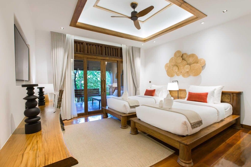 ห้องนอนกว้างขวางพร้อมการออกแบบสไตล์ทรอปิคอลสมัยใหม่ มีเพดานสูง เตียงขนาดใหญ่ โซฟาสีขาว และตกแต่งด้วยไม้ ที่พักมวกเหล็ก