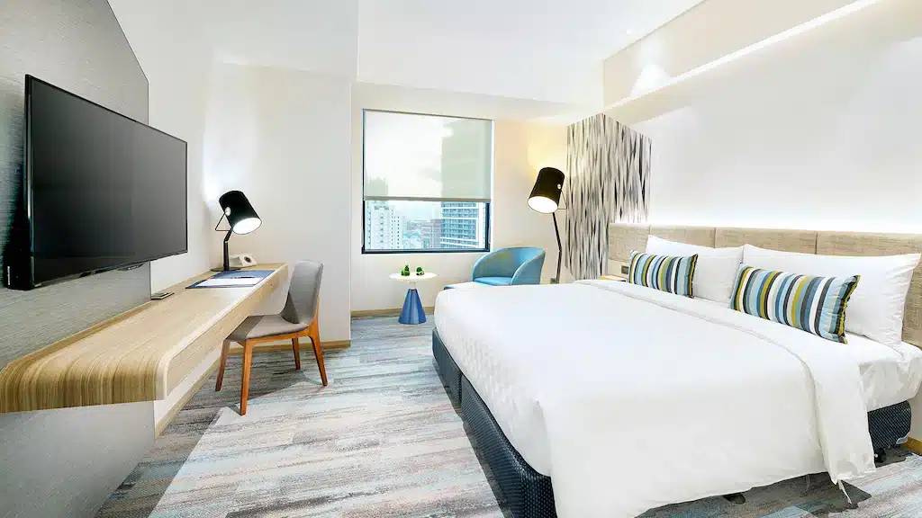 ห้องพักโรงแรมทันสมัยพร้อมเตียงขนาดใหญ่ พื้นที่โต๊ะ ที่เที่ยวไต้หวัน และวิวเมืองผ่านหน้าต่างในราชบุรี